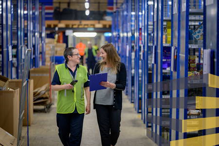 Two people walking in a warehouse to illustrate article about warehouse work stations